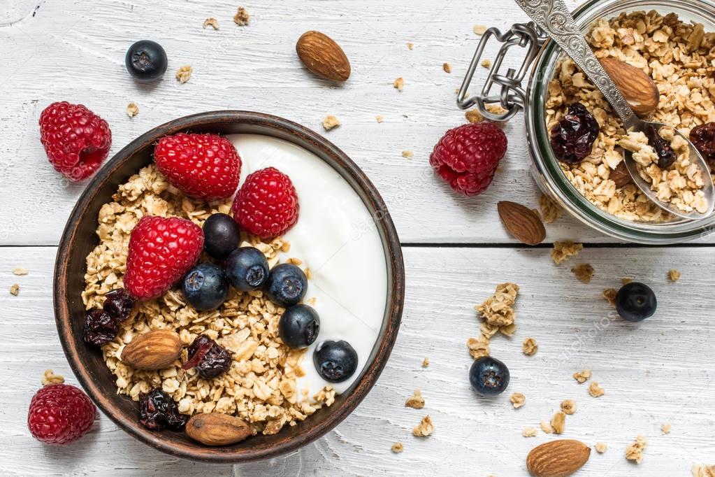 bowl of oat granola with yogurt, fresh raspberries, blueberries and nuts