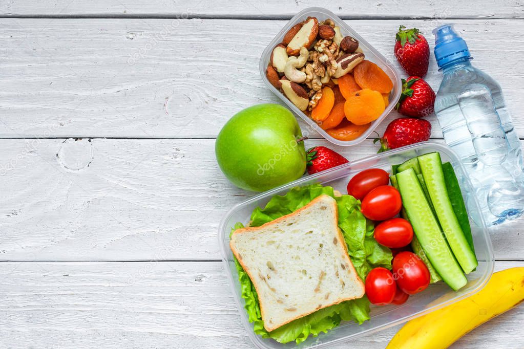 school lunch boxes with sandwich and fresh vegetables, bottle of water, nuts and fruits