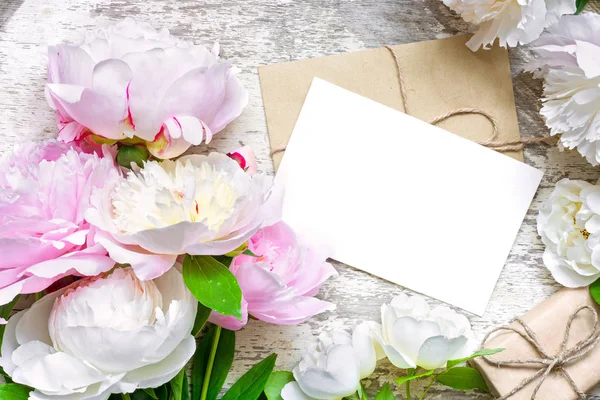Tarjeta de felicitación blanca en blanco y sobre con caja de regalo en marco de peonías y rosas flores — Foto de Stock