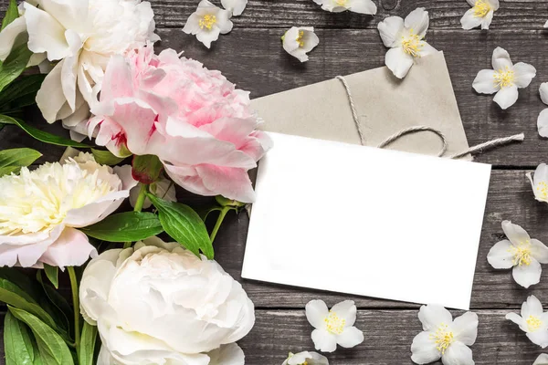 Blank greeting card and envelope in frame of pink and white peonies and jasmine flowers — Stock Photo, Image