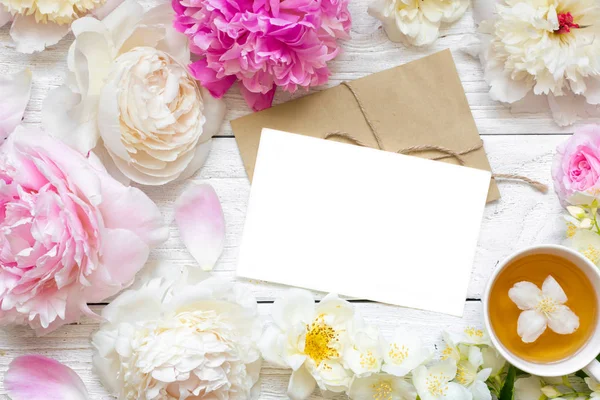 Tarjeta de felicitación en blanco o invitación a la boda con tiernas peonías y rosas flores con taza de té de jazmín verde — Foto de Stock