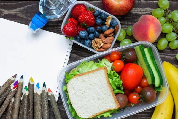 学校午餐饭盒与三明治、 水果、 蔬菜和瓶水彩色的铅笔与空本抄写本 — 图库照片