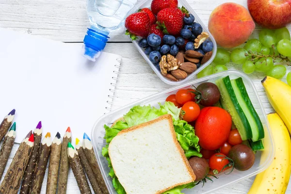 School lunch boxes with sandwich, fruits, vegetables and bottle of water with colored pencils — Stock Photo, Image