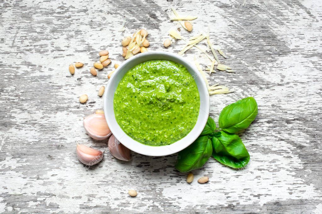 Pesto sauce in a bowl with pine nuts, parmesan and garlic over rustic wooden background