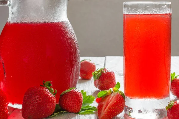 Jugo de fresa fría en un vaso y jarra sobre una mesa de madera blanca —  Fotos de Stock