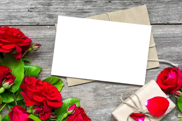 Bukett röda rosor med en tom gratulationskort och kuvert med presentask — Stockfoto