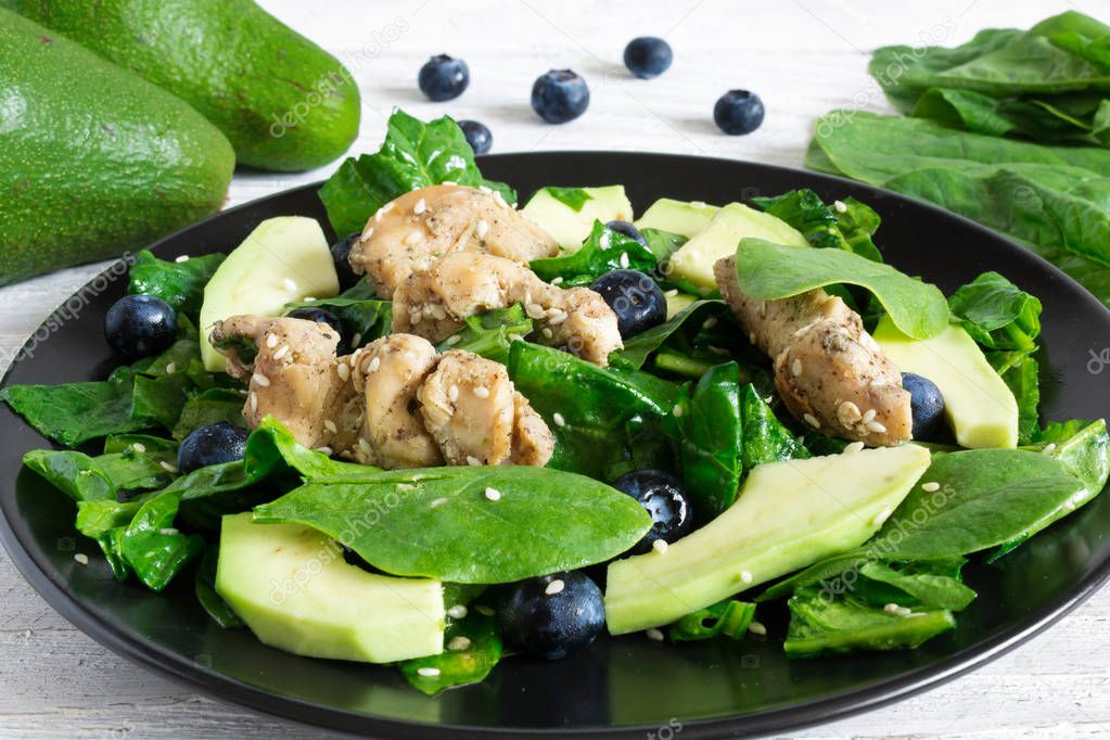 Chicken salad with avocado, spinach and blueberries in black plate