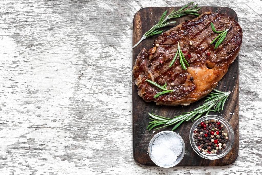 Grilled beef steak with herbs and spices on wooden cutting board