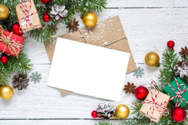 Noel tebrik kartı köknar ağacı dalları, süslemeleri ve hediye kutuları Beyaz ahşap zemin üzerinde