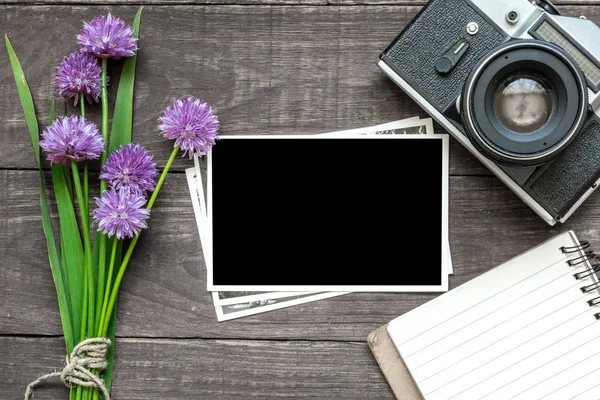 Вінтажна ретро-камера з порожньою фоторамкою, фіолетовими дикими квітами та вишитим блокнотом на сільському дерев'яному фоні — стокове фото