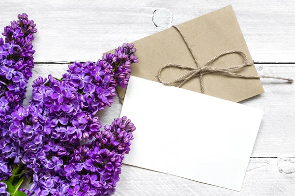 Blank vit gratulationskort och kuvert med lila blommor över vit trä bakgrund — Stockfoto