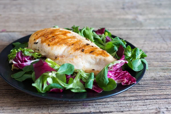 Filete de pollo a la parrilla con ensalada mixta en un plato negro —  Fotos de Stock