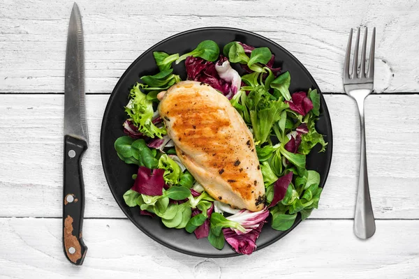 Gegrilde Kipfilet met gemengde salade op een zwarte plaat met mes en vork — Stockfoto