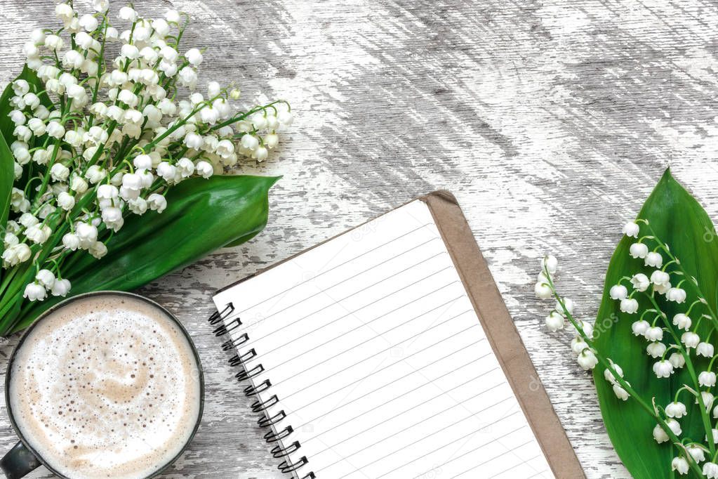 cup of cappuccino with spring lily of the valley flowers and lined notebook