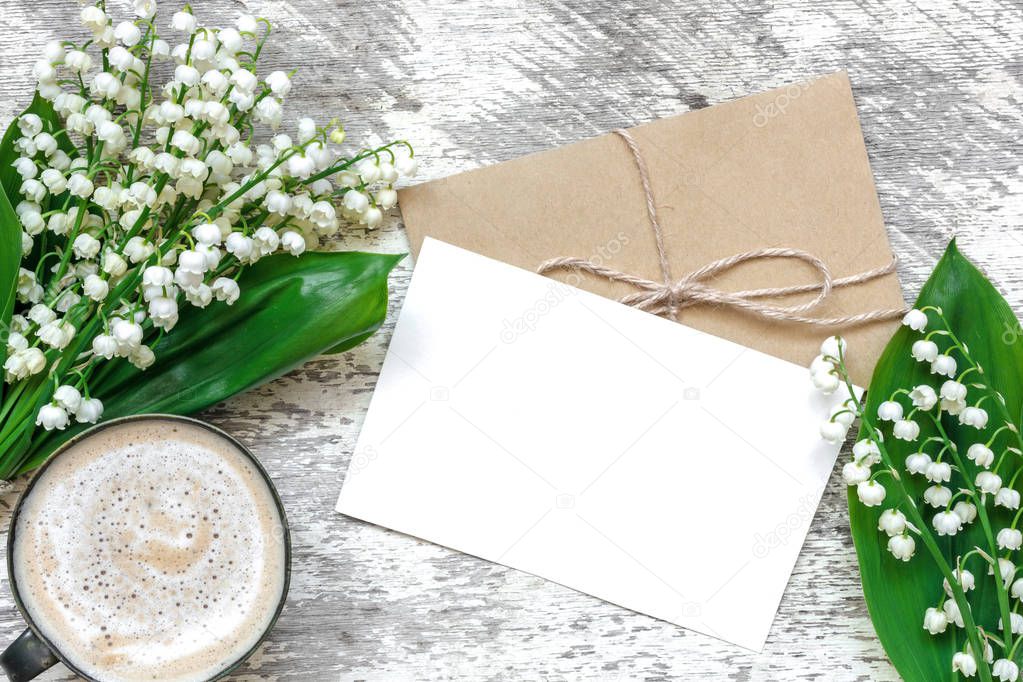 cup of cappuccino with blank white greeting card and envelope with spring lily of the valley flowers