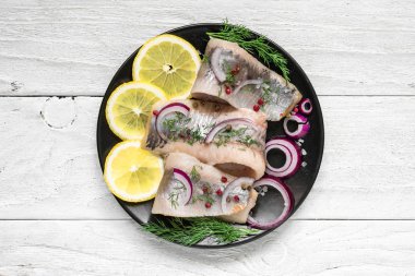 Tuz, biber, otlar, soğan ve beyaz arka plan üzerinde siyah plaka üzerinde limon ile ringa balığı filetosu