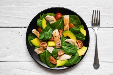 Avokado, ıspanak ve domates kiraz çatal ile siyah plaka Tavuk salatası