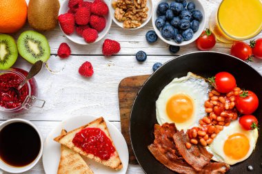 İngiliz kahvaltısı - kızarmış yumurta, fasulye, domates, kahve, pastırma ve portakal suyu, taze meyve ve çilek ile tost