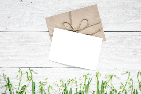 Puste białą kartkę z życzeniami z wiosennych kwiatów przebiśnieg nad biały drewniany stół — Zdjęcie stockowe