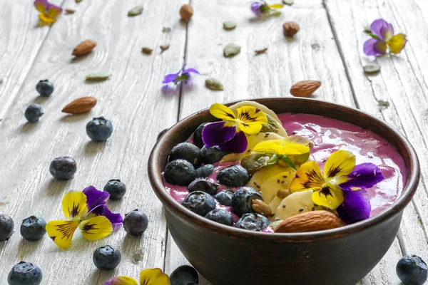 Ciotola di frullato condita con bacche fresche, banana, semi di chia, noci e fiori per una sana colazione vegetariana . — Foto Stock