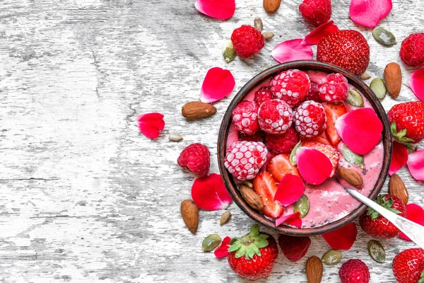 Sarapan sehat. semangkuk berry smoothie merah dengan stroberi, raspberry, kacang-kacangan dan biji-bijian dihiasi dengan kelopak bunga mawar — Stok Foto