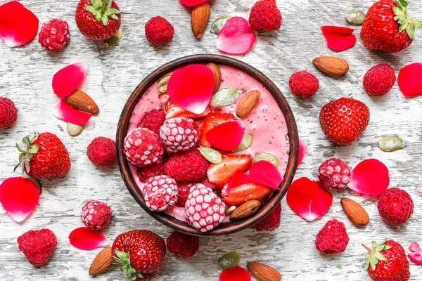 Tazón de batido con bayas rojas - fresa y frambuesa congelada, frutos secos, semillas y pétalos de flores de rosas — Foto de Stock