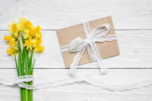 Чистая белая открытка и конверт с весенне-желтым нарциссом букет цветов над белым деревянным столом — стоковое фото