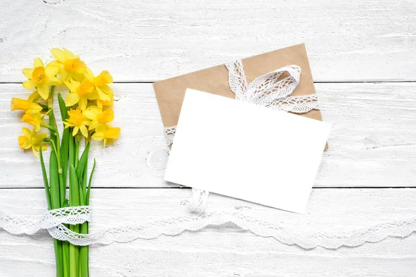 Bahar sarı nergis çiçek kokulu beyaz ahşap masa üzerinde boş beyaz tebrik kartı. yukarı alay. — Stok fotoğraf
