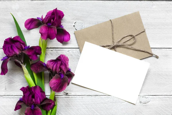 Mor Iris çiçek buketi ve zarf Beyaz ahşap zemin üzerinde boş beyaz tebrik kartı — Stok fotoğraf