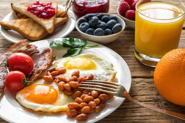 Сніданок, включаючи апельсиновий сік, смажене яйце, бекон, квасоля, фрукти та ягоди . — стокове фото