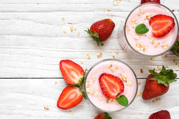 Yogur de fresa saludable con avena y menta en vasos con bayas frescas sobre una mesa de madera blanca — Foto de Stock