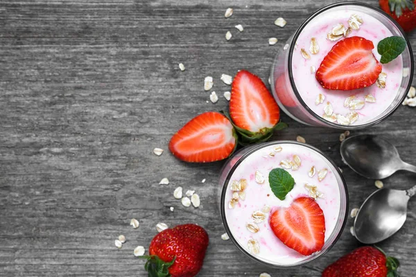 Yogurt de fresa con avena y menta en vasos con bayas frescas y cucharas sobre mesa de madera blanca — Foto de Stock