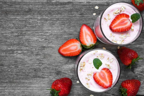 Yogur de fresa saludable con avena y menta en vasos con bayas frescas sobre una mesa de madera rústica — Foto de Stock