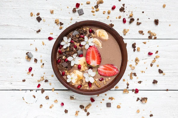 cocoa banana protein smoothie bowl with chocolate granola, strawberry and pomegranate seeds decorated with flowers