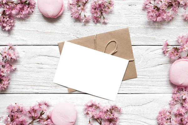 Tarjeta de felicitación en blanco o invitación a la boda en marco de flor de cerezo rosa o sakura sobre mesa de madera blanca — Foto de Stock