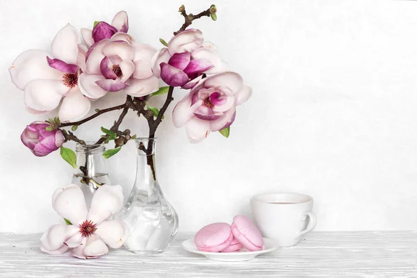 Букет цветов розовой магнолии с чашкой кофе и макаронами на белом деревянном фоне — стоковое фото