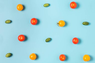 Mavi arka planda küçük salatalıklar, sarı ve kırmızı domatesler. düz yat