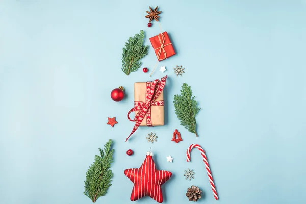 크리스마스 트리는 전나무 가지, 빨간 장식, 사탕, 겨울 베리, 파란 배경의 선물 상자들로 만들어 진다 — 스톡 사진