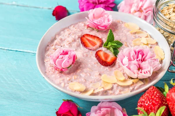 overnight oats with fresh strawberries, almonds and mint in a bowl with rose flowers on blue wooden table
