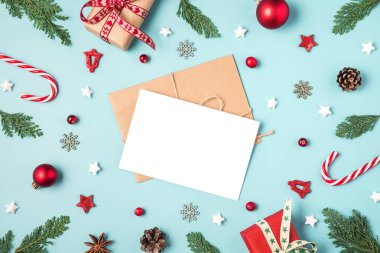 Çam ağacının dallarından, hediye kutularından, şekerlerden, mavi arka planda kırmızı süslemelerden oluşan çerçevedeki Noel tebrik kartı.