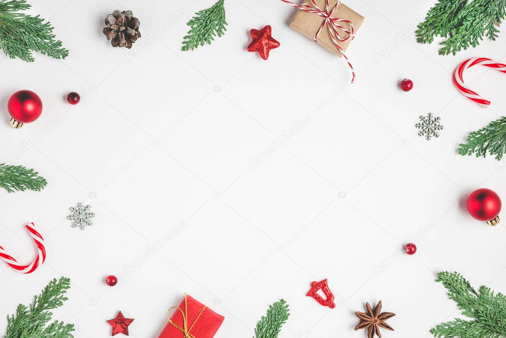 Christmas frame made of fir branches, gift boxes, candy, red holiday decorations and pine cones on white background