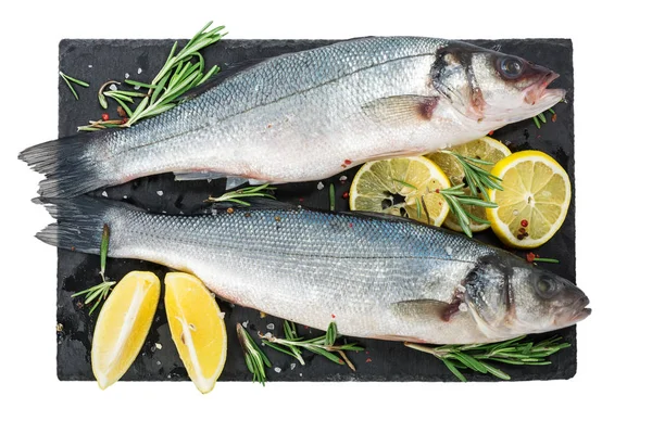 Pescado fresco de lubina e ingredientes para cocinar, limón, pimienta y romero sobre pizarra negra aislada sobre fondo blanco —  Fotos de Stock