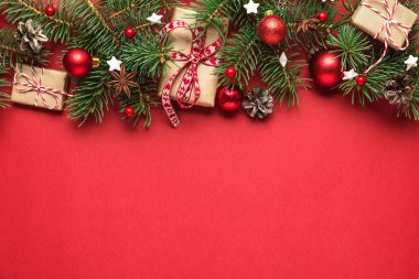 Noel ya da Mutlu Yıllar kompozisyonu. Firavun dalları, çam kozalakları, hediye kutuları ve kırmızı arka planda tatil süslemeleri.