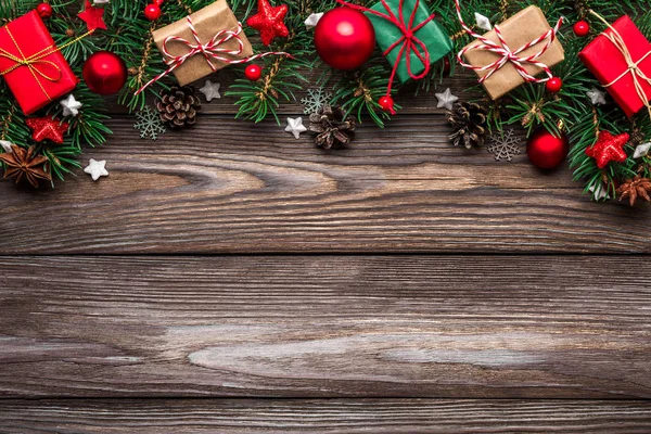 Vánoční zázemí s jedlovými větvemi, dekoracemi, dárkovými krabicemi a borovými kužely na venkovském dřevěném stole. pohled shora — Stock fotografie