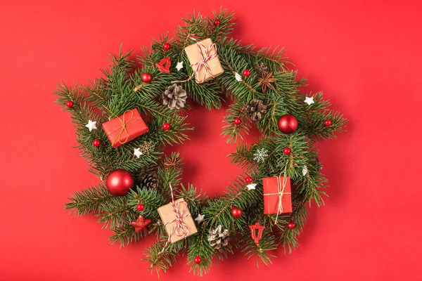 Corona de Navidad hecha de ramas de abeto, decoraciones rojas, cajas de regalo, conos de pino sobre fondo rojo —  Fotos de Stock