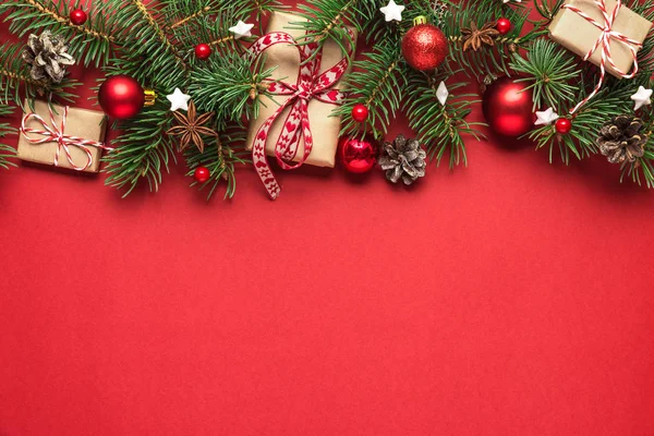 Noel ya da Mutlu Yıllar kompozisyonu. Firavun dalları, çam kozalakları, hediye kutuları ve kırmızı arka planda tatil süslemeleri.