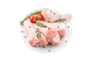 Çiğ tavuk budu ya da bacakları beyaz arka planda izole edilmiş bitki ve baharatlarla dolu bir tabakta.