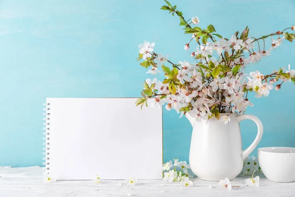 Νεκρή φύση με όμορφα ανοιξιάτικα άνθη κερασιάς, φλιτζάνι καφέ και λευκή ευχετήρια κάρτα σε μπλε φόντο. μακιγιάρισμα — Φωτογραφία Αρχείου