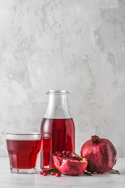 Botella de jugo de granada con un vaso de jugo y frutas frescas de granada sobre una mesa de mármol. Orientación vertical — Foto de Stock