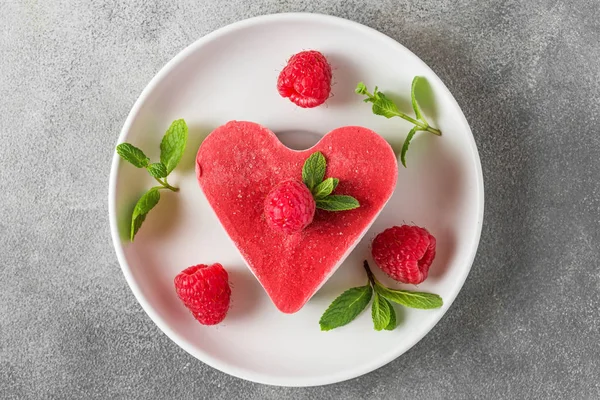 Postre de San Valentín. pastel rojo vegano crudo en forma de corazón con frambuesas y menta en un plato. comida deliciosa saludable — Foto de Stock